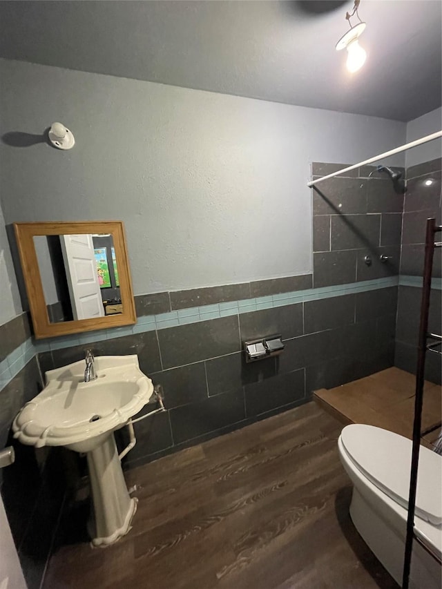 bathroom featuring hardwood / wood-style flooring, a tile shower, tile walls, and toilet