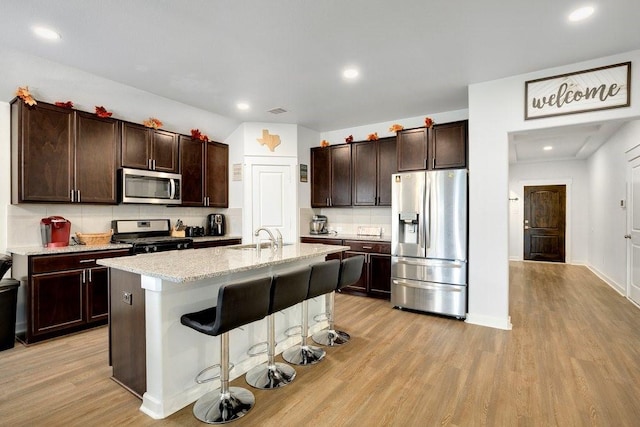 kitchen with sink, light hardwood / wood-style flooring, stainless steel appliances, an island with sink, and a kitchen bar