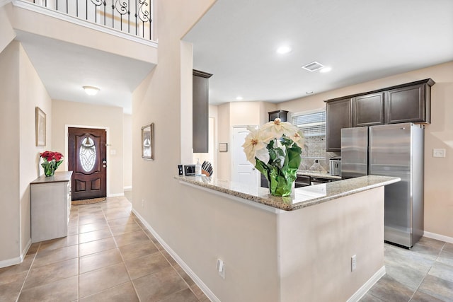 kitchen featuring a wealth of natural light, stainless steel fridge, light stone countertops, and kitchen peninsula