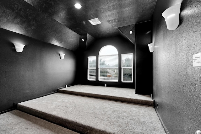 carpeted home theater room with vaulted ceiling and a textured ceiling