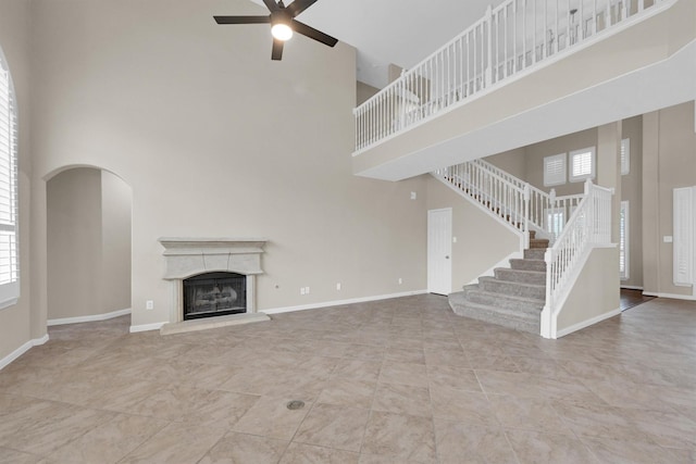 unfurnished living room with ceiling fan, a healthy amount of sunlight, and a high ceiling