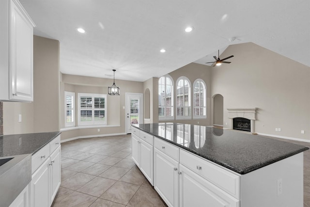 kitchen with dark stone countertops, a kitchen island, pendant lighting, ceiling fan with notable chandelier, and white cabinets