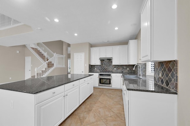 kitchen with dark stone countertops, oven, sink, and white cabinets