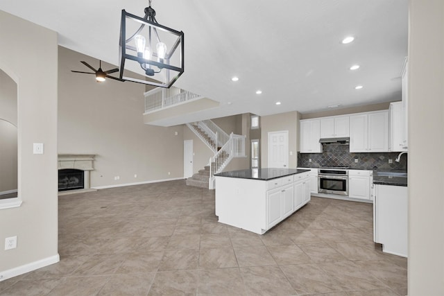 kitchen with tasteful backsplash, stainless steel oven, decorative light fixtures, a kitchen island, and white cabinets