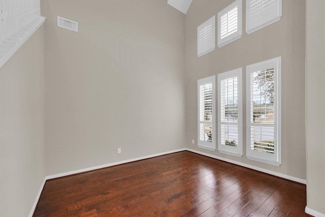 unfurnished room featuring a towering ceiling and dark wood-type flooring