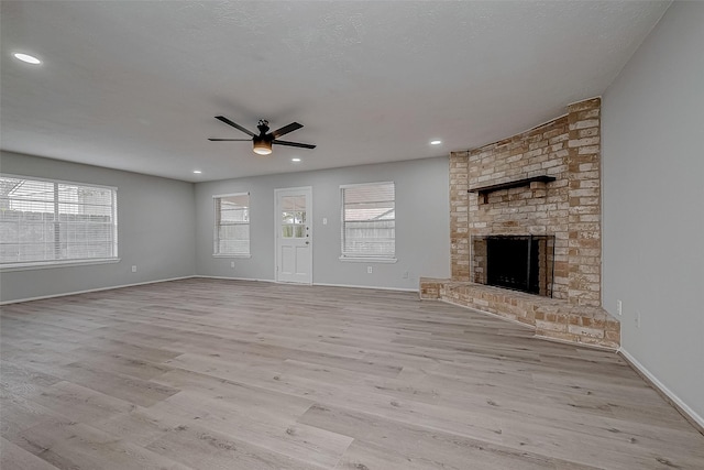 unfurnished living room with ceiling fan, a textured ceiling, a fireplace, and light hardwood / wood-style flooring