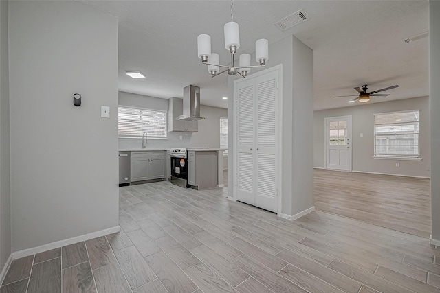 kitchen with gray cabinets, appliances with stainless steel finishes, decorative light fixtures, plenty of natural light, and wall chimney range hood