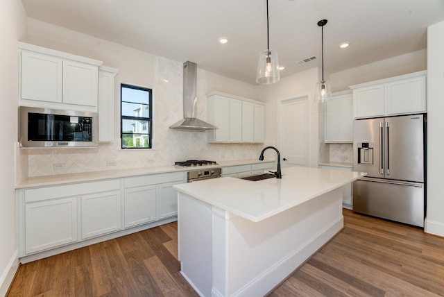 kitchen with wall chimney exhaust hood, sink, appliances with stainless steel finishes, a kitchen island with sink, and white cabinets