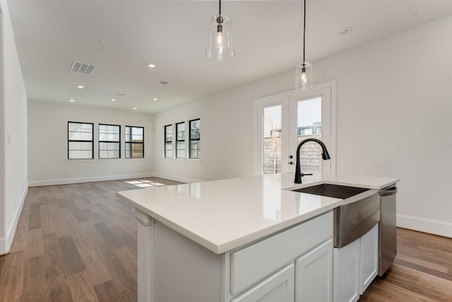 kitchen with white cabinets, a healthy amount of sunlight, hanging light fixtures, and a center island with sink