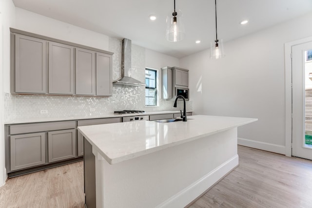 kitchen with sink, gray cabinetry, backsplash, hanging light fixtures, and wall chimney range hood