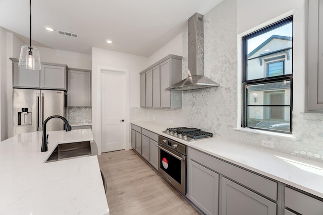 kitchen featuring sink, hanging light fixtures, stainless steel appliances, light stone countertops, and wall chimney range hood