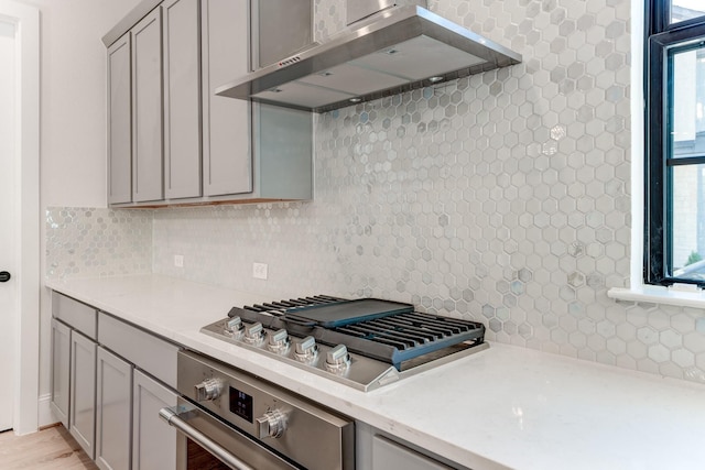 kitchen with stainless steel appliances, gray cabinets, decorative backsplash, and wall chimney exhaust hood