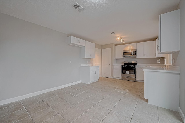 kitchen featuring sink, appliances with stainless steel finishes, white cabinetry, a textured ceiling, and light tile patterned flooring