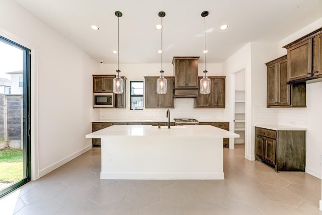 kitchen with built in microwave, decorative light fixtures, an island with sink, and dark brown cabinets