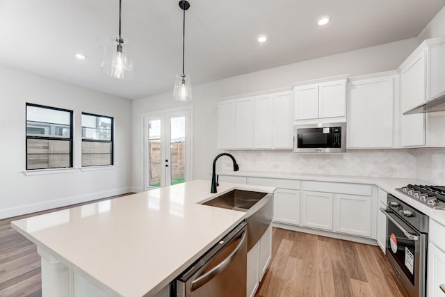 kitchen with white cabinets, hanging light fixtures, stainless steel appliances, a center island with sink, and french doors