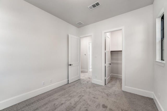 unfurnished bedroom with light carpet and a walk in closet