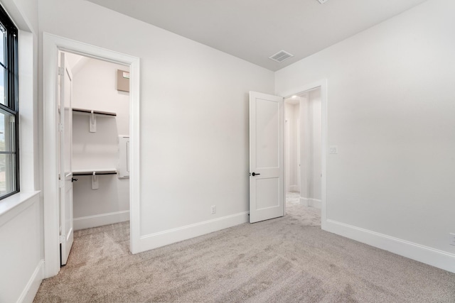 unfurnished bedroom featuring a spacious closet, light carpet, and a closet