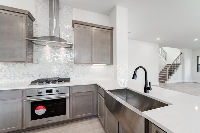 kitchen with sink, tasteful backsplash, light hardwood / wood-style flooring, stainless steel appliances, and wall chimney range hood