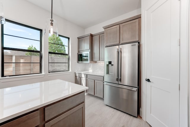 kitchen with high quality fridge, light hardwood / wood-style flooring, backsplash, and decorative light fixtures