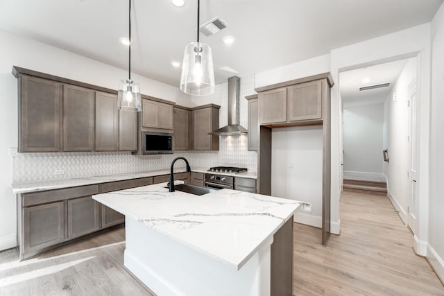 kitchen with pendant lighting, sink, stainless steel appliances, light stone countertops, and wall chimney range hood