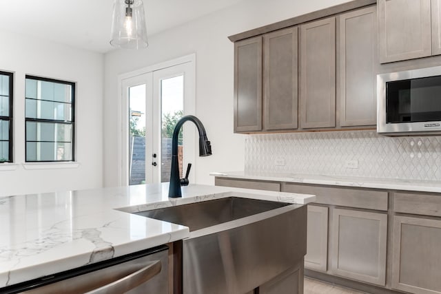 kitchen featuring hanging light fixtures, light stone countertops, sink, and backsplash