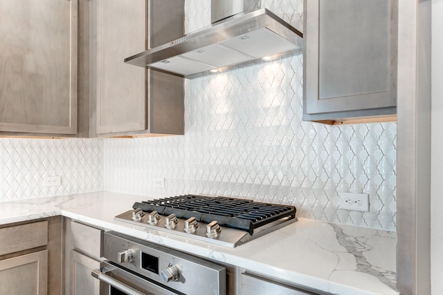 kitchen featuring light stone counters, wall chimney exhaust hood, stainless steel appliances, and backsplash