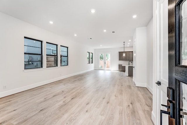 unfurnished living room featuring french doors, sink, and light hardwood / wood-style flooring