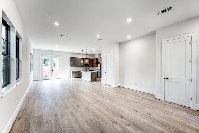 unfurnished living room with sink, light hardwood / wood-style floors, and french doors