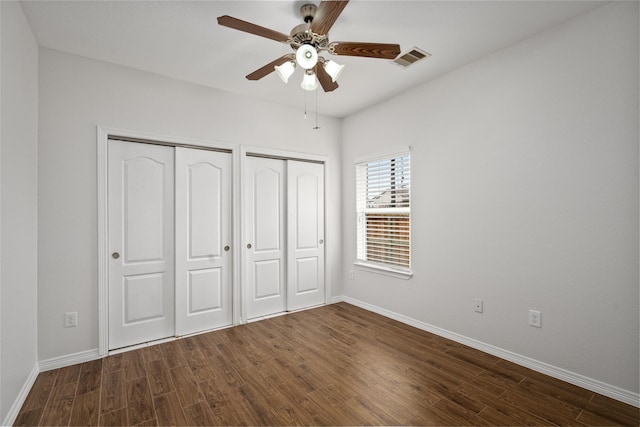 unfurnished bedroom featuring multiple closets, ceiling fan, and dark hardwood / wood-style floors