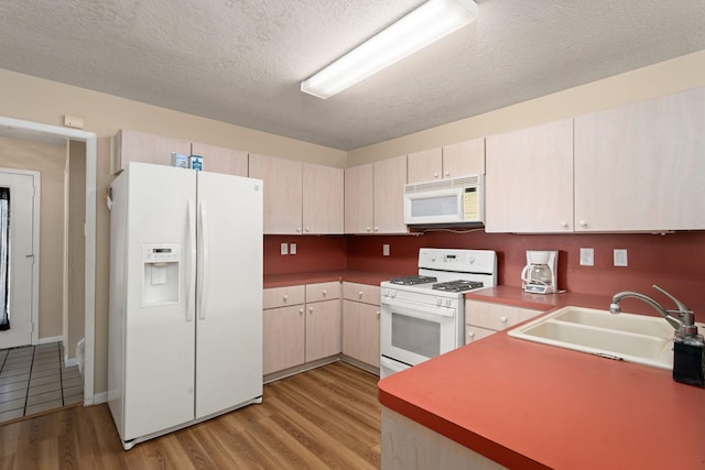 kitchen featuring sink, white appliances, light hardwood / wood-style floors, and a textured ceiling