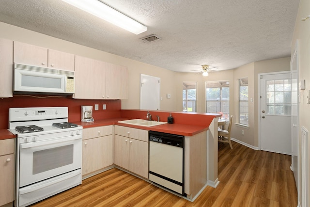 kitchen featuring sink, wood-type flooring, a textured ceiling, kitchen peninsula, and white appliances