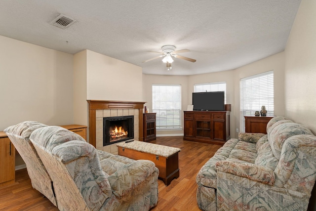 living room with ceiling fan, light hardwood / wood-style floors, a tile fireplace, and a textured ceiling