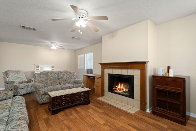 living room with dark hardwood / wood-style flooring, ceiling fan, a tiled fireplace, and a textured ceiling