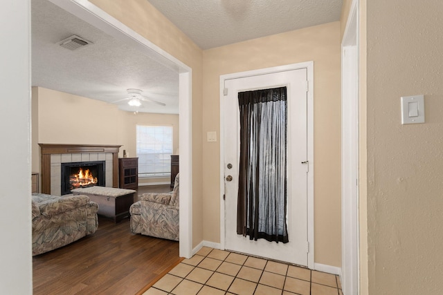 entryway with ceiling fan, a tile fireplace, light hardwood / wood-style floors, and a textured ceiling