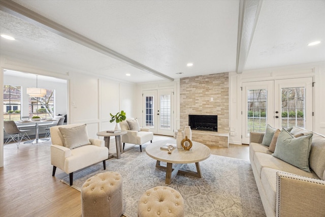 living room featuring french doors, light wood-type flooring, a textured ceiling, and beamed ceiling