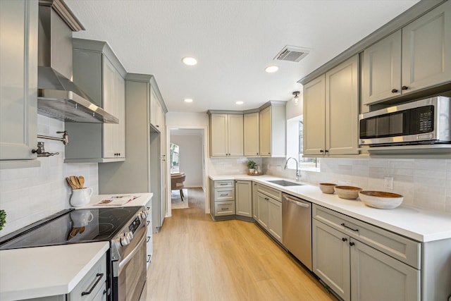 kitchen with gray cabinets, appliances with stainless steel finishes, and wall chimney range hood