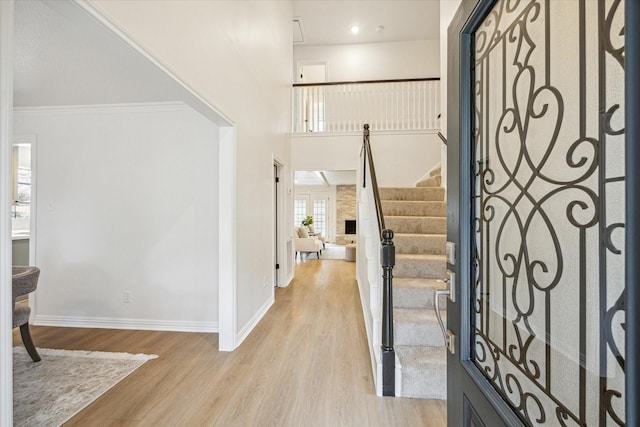 entryway featuring a towering ceiling, ornamental molding, and light hardwood / wood-style flooring