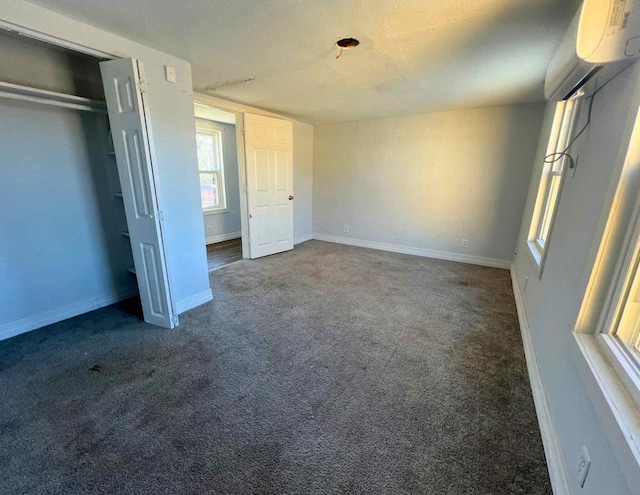 unfurnished bedroom with dark colored carpet, an AC wall unit, and a closet