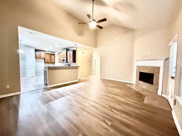 unfurnished living room featuring a tile fireplace, ceiling fan, high vaulted ceiling, and light hardwood / wood-style floors