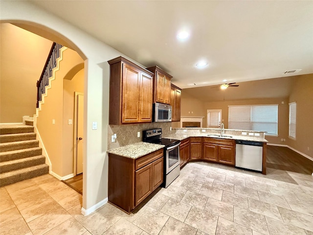 kitchen featuring sink, appliances with stainless steel finishes, light stone counters, decorative backsplash, and kitchen peninsula