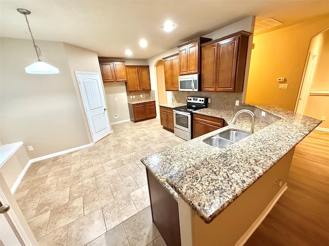 kitchen featuring appliances with stainless steel finishes, pendant lighting, sink, decorative backsplash, and kitchen peninsula