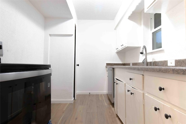 kitchen with stainless steel dishwasher, sink, light hardwood / wood-style floors, and white cabinets