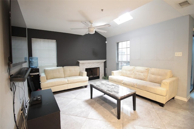 living room with ceiling fan, light tile patterned floors, a fireplace, and vaulted ceiling with skylight