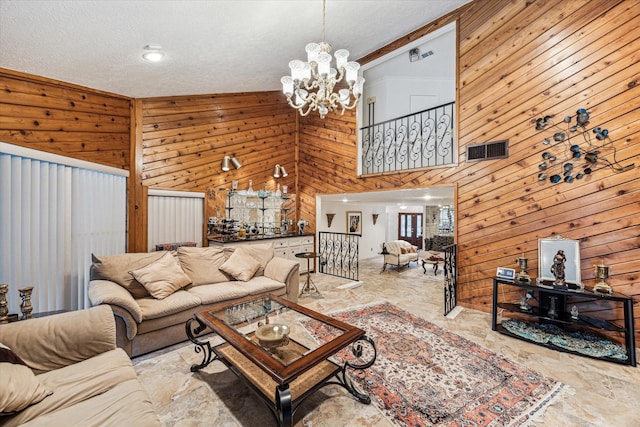 living room featuring a notable chandelier, a towering ceiling, and wooden walls