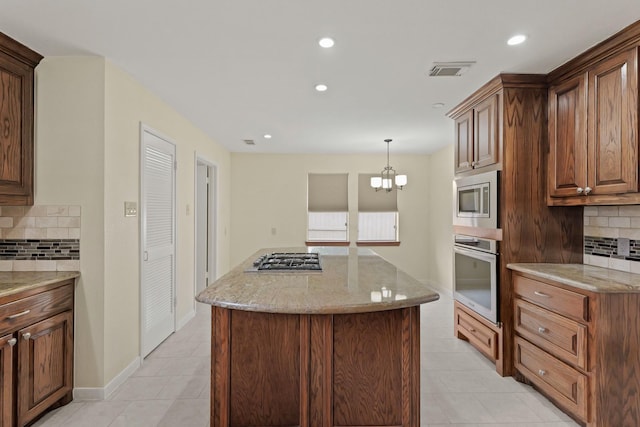 kitchen with hanging light fixtures, light stone countertops, appliances with stainless steel finishes, and a center island