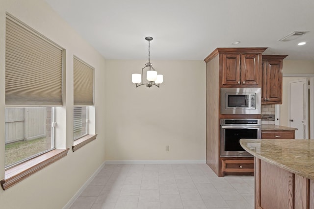 kitchen featuring appliances with stainless steel finishes, tasteful backsplash, a notable chandelier, light stone counters, and decorative light fixtures