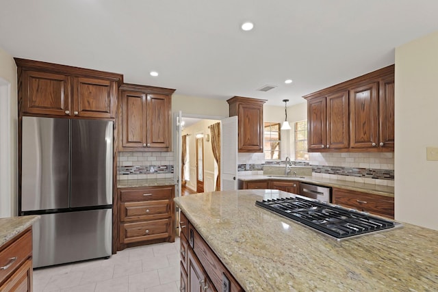 kitchen featuring appliances with stainless steel finishes, pendant lighting, tasteful backsplash, sink, and light stone counters