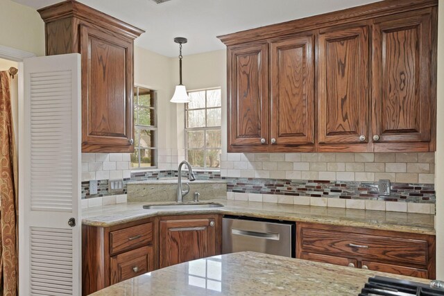 kitchen with pendant lighting, sink, stainless steel dishwasher, and light stone countertops