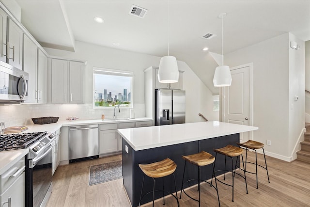 kitchen featuring a kitchen island, decorative light fixtures, sink, stainless steel appliances, and light wood-type flooring