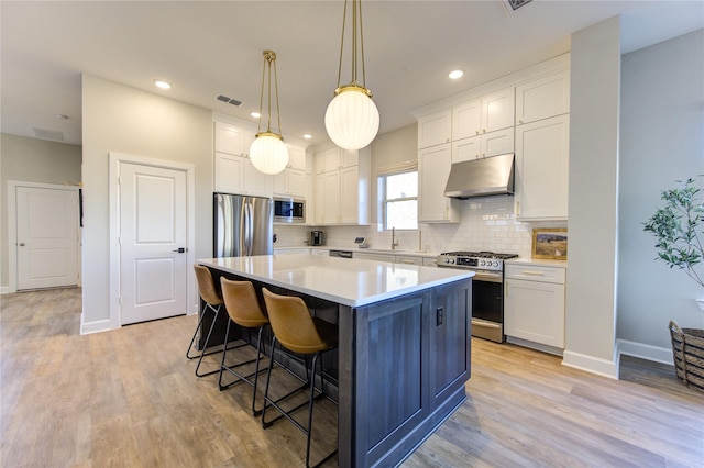 kitchen with appliances with stainless steel finishes, decorative light fixtures, white cabinets, a center island, and light hardwood / wood-style flooring